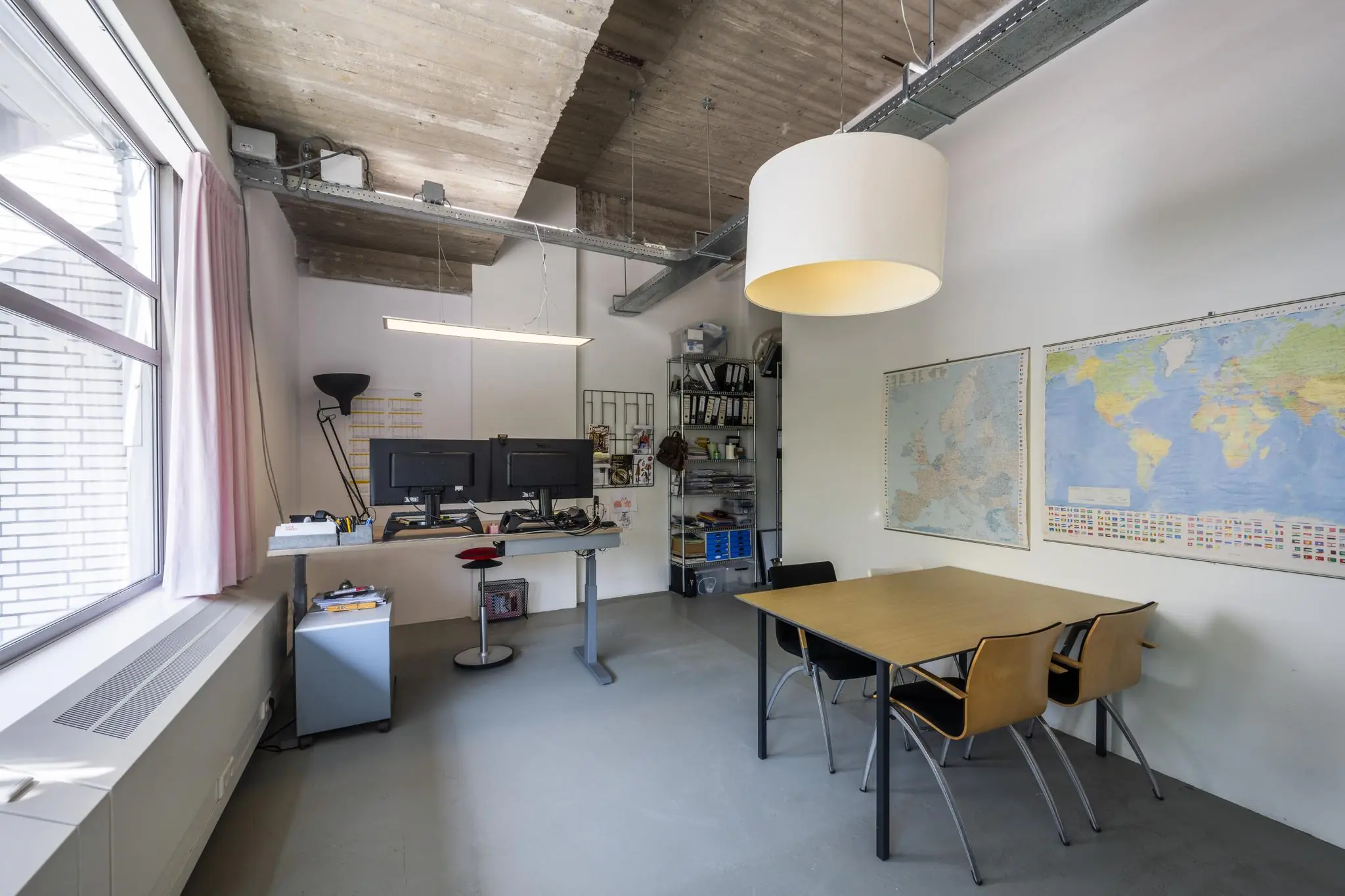 Moderne kantoorruimte aan de Van Leijenberghlaan met een zitgedeelte, sta-bureau, wereldkaarten aan de muur en industriële plafondafwerking.